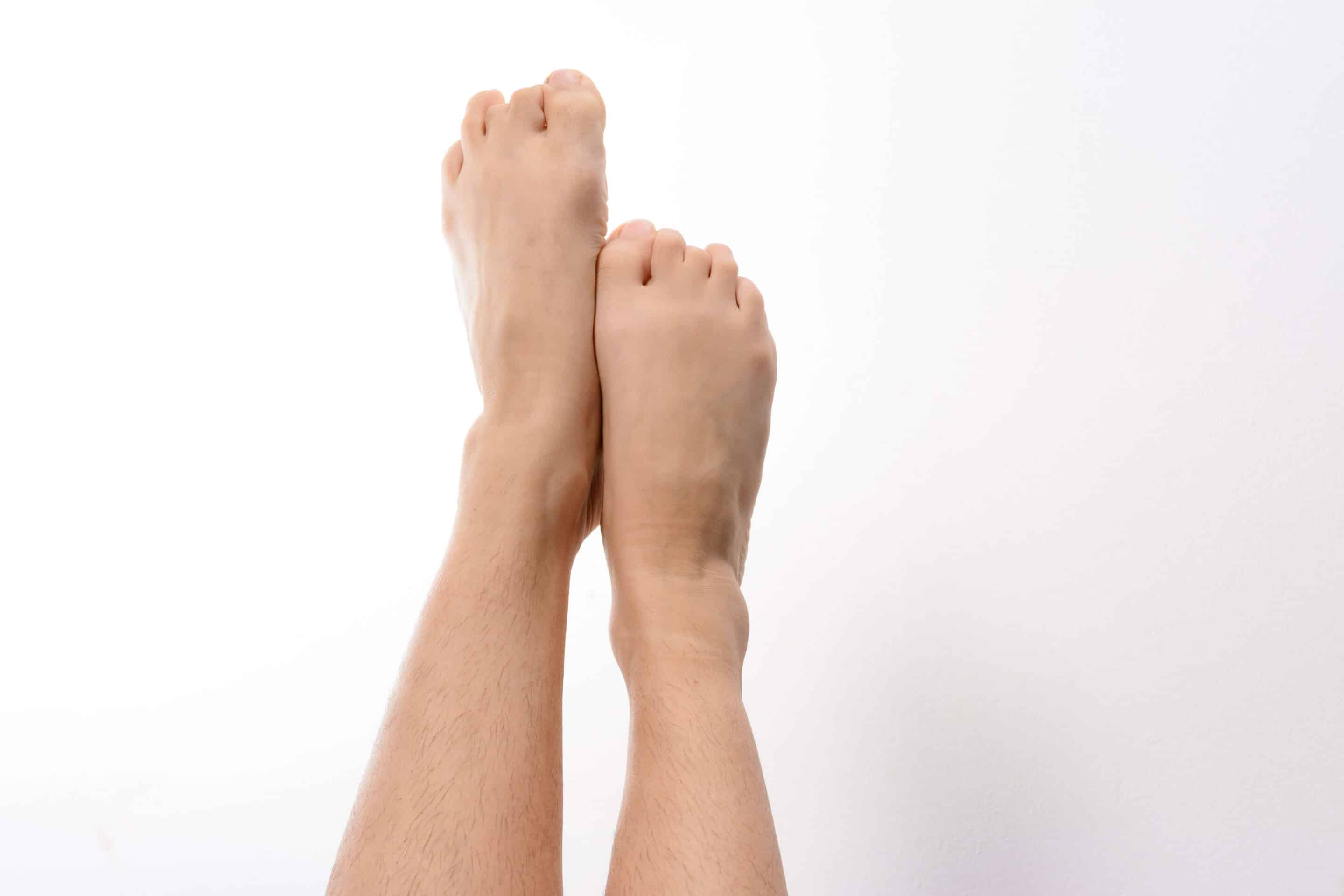 Close-up of a pair of clean feet raised against a plain white background. The image focuses on the details of the skin and toes.